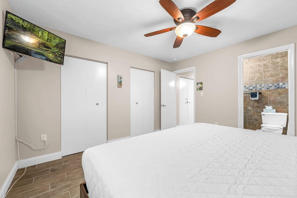 Bedroom with ceiling fan, wall-mounted TV, and direct access to a tiled bathroom.