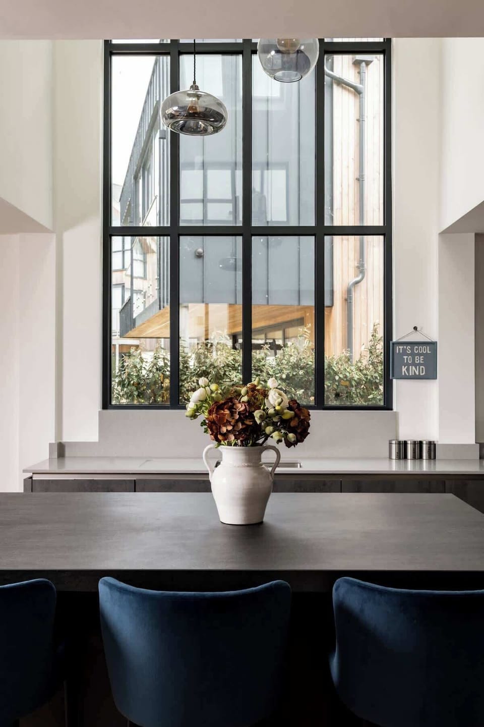 Framed by double-height windows, the kitchen is a space of calm, light, and quiet intention.