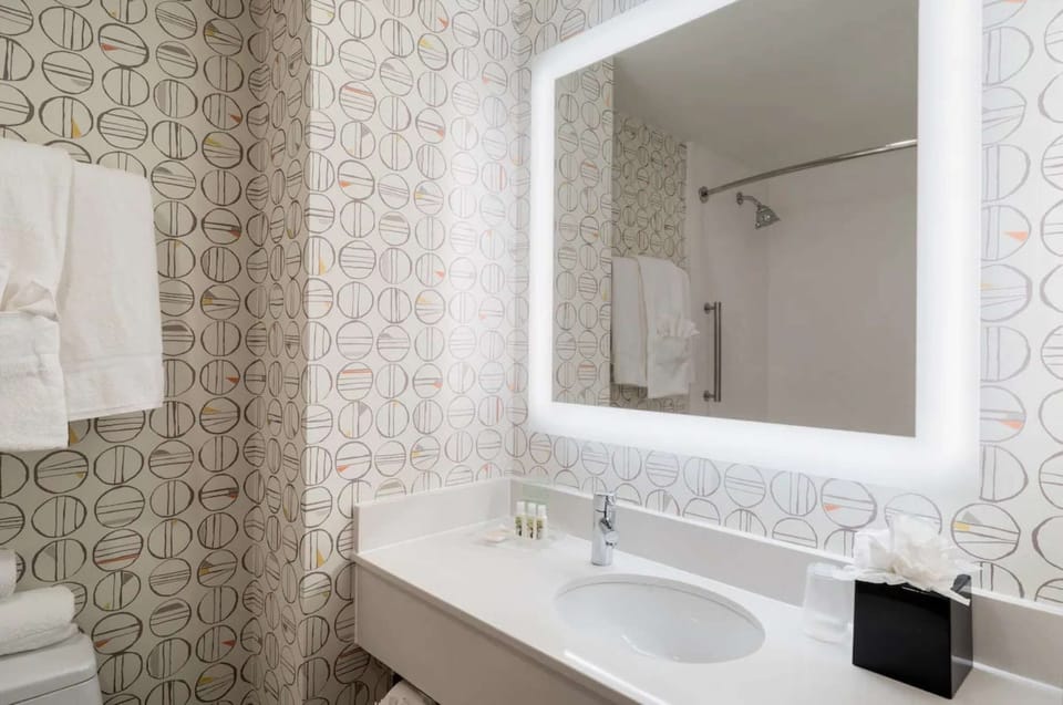 Bathroom with circle-print wallpaper and bright lighted mirror