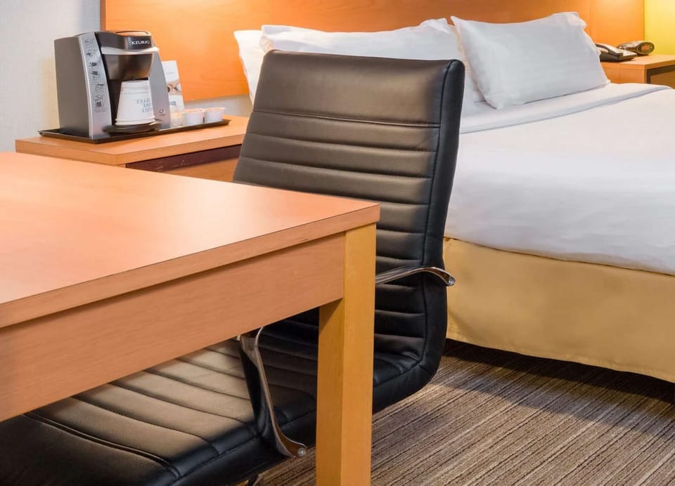 Desk and black chair near bed with Keurig coffee maker