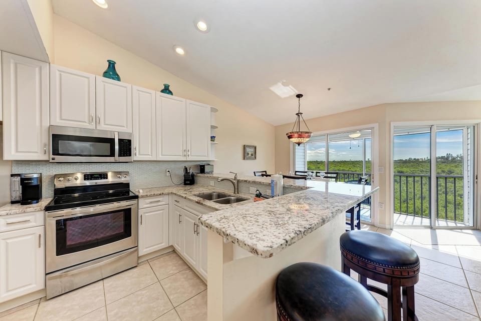 Your fully-equipped kitchen features granite countertops, stainless steel appliances, and a breakfast bar with stunning nature views through floor-to-ceiling windows.