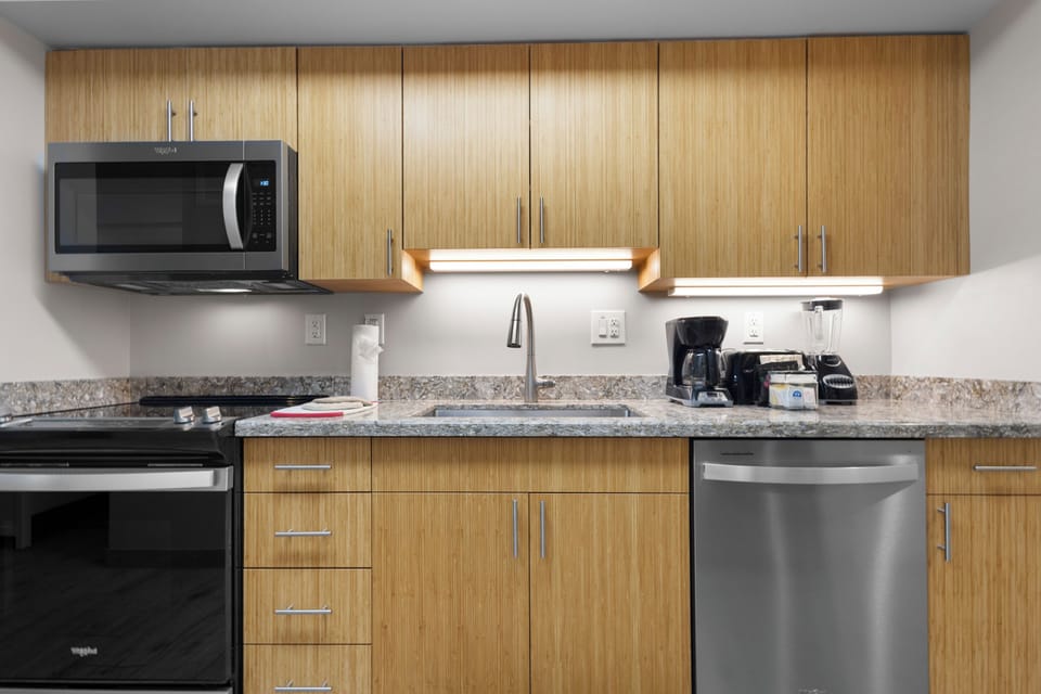 Your modern kitchen features sleek wood cabinetry, granite counters, and stainless appliances including microwave, dishwasher, and coffee maker—perfect for preparing meals during your stay.