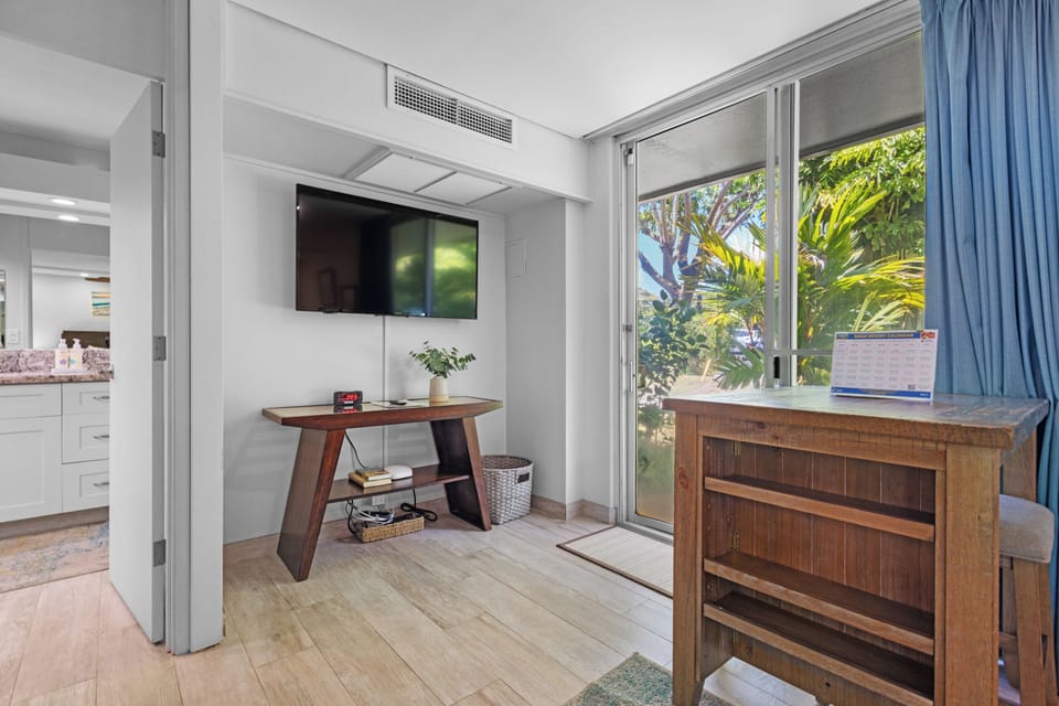 Your cozy retreat features a flat-screen TV, elegant furnishings, and doors opening to lush tropical greenery for a refreshing escape.