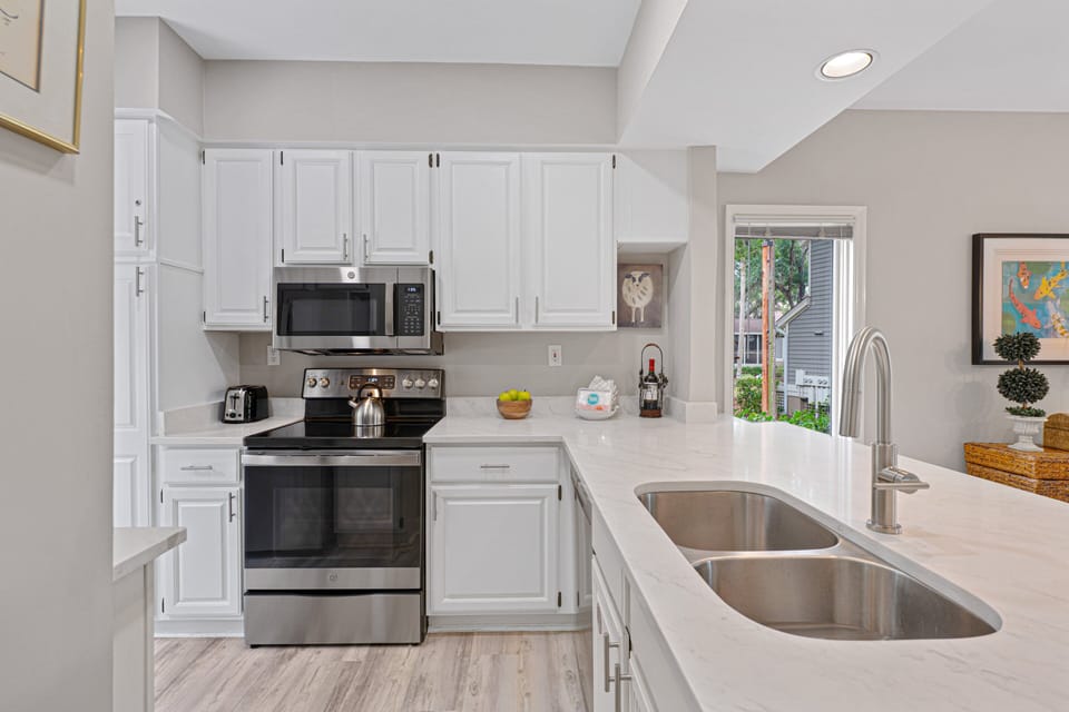 This clean, updated kitchen features white cabinetry, solid-surface countertops, and stainless steel appliances including a smooth-top range and built-in microwave.