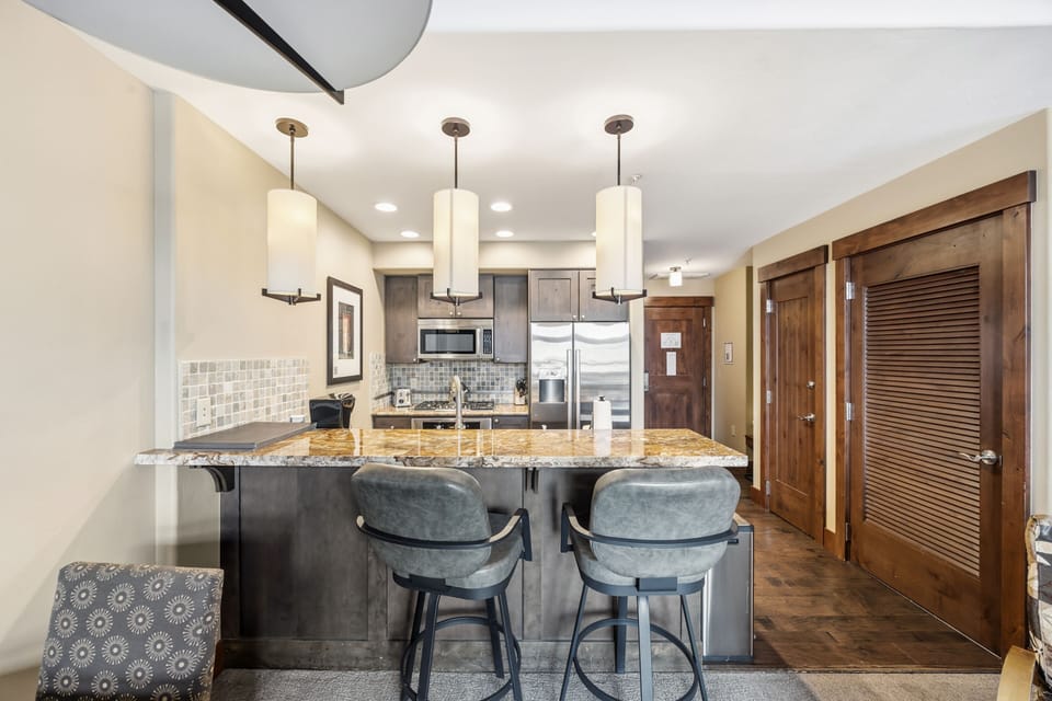 Breakfast bar — granite, drum pendants, channel-tufted stools.
