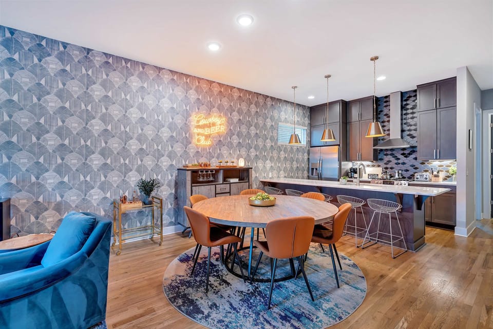 Dining room with neon sign and kitchen view beyond, bringing a playful energy to family-style meals before everyone scatters