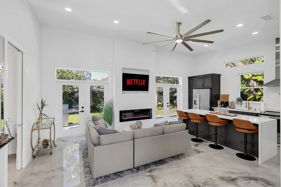 Modern open living area with a large sectional sofa, kitchen island seating, and natural light from multiple windows.