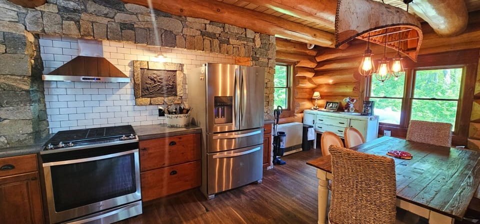 Rustic log cabin kitchen with stone accents, stainless steel appliances, and dining table.