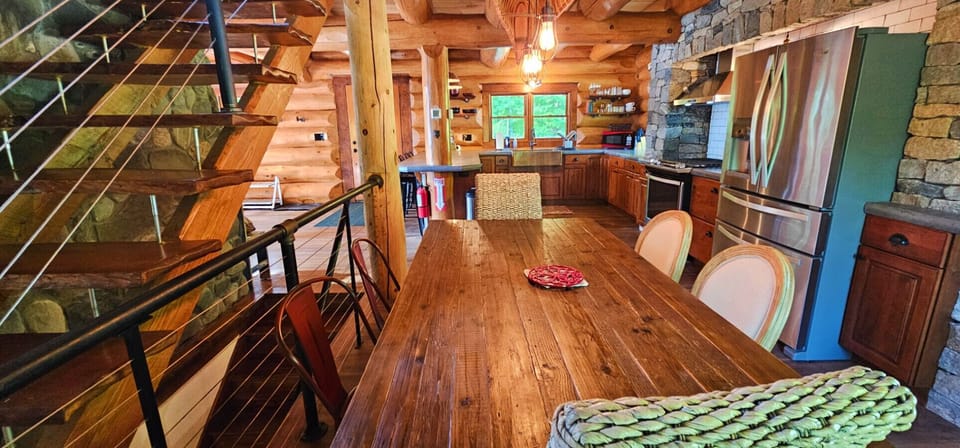 Spacious log cabin dining area with a handcrafted wood table, rustic staircase, and fully equipped kitchen for memorable gatherings.