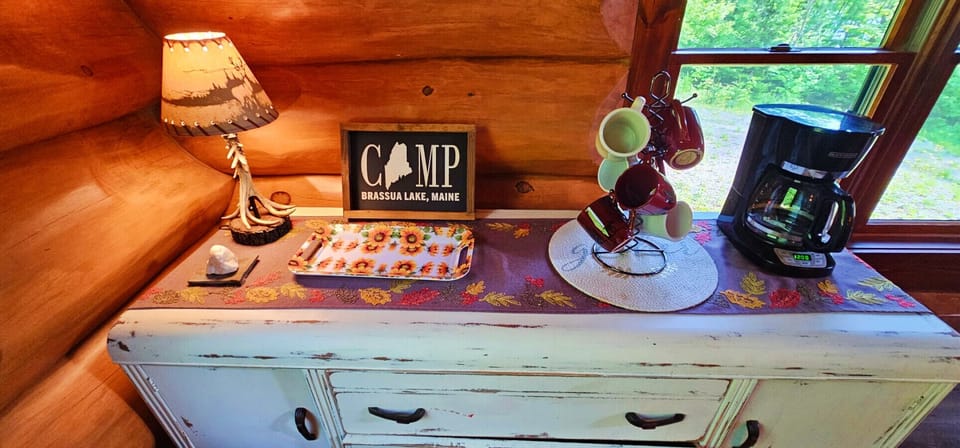 Rustic coffee station with a drip coffee maker, colorful mugs, and cozy cabin charm overlooking the woods.
