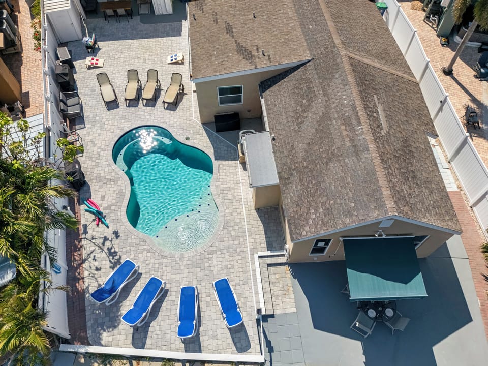 Aerial view of backyard oasis with pool, loungers, grill, and waterfront dock.
