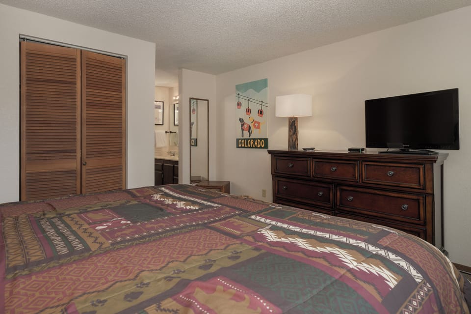 Your cozy bedroom features rustic charm with southwestern-patterned bedding, rich wood furniture, and modern conveniences like TV for relaxing mountain getaway evenings.