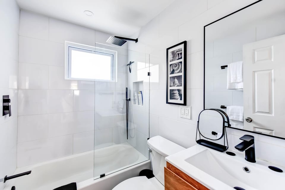 Relax in a sleek modern bathroom featuring a soaking tub with a glass shower door, 
black fixtures, premium toiletries, and thoughtful touches like framed art and a large 
mirror.