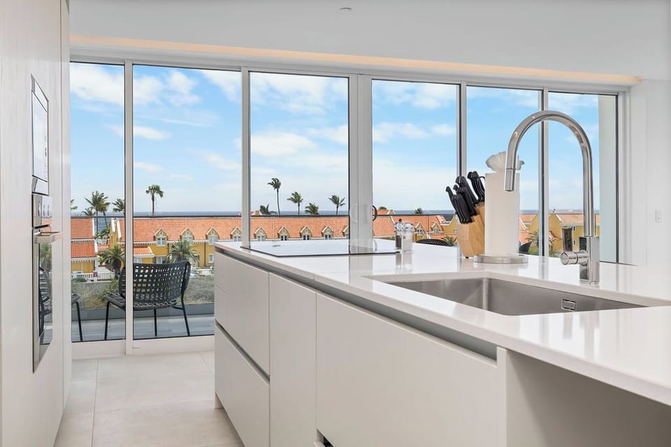 Your sleek, sunlit kitchen awaits, featuring pristine countertops and modern appliances, with gorgeous ocean views framing your cooking space through expansive windows.
