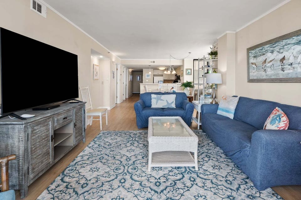 Blue sofas and a patterned rug face the wall-mounted TV at Sea Pointe 702 in Cherry Grove, North Myrtle Beach