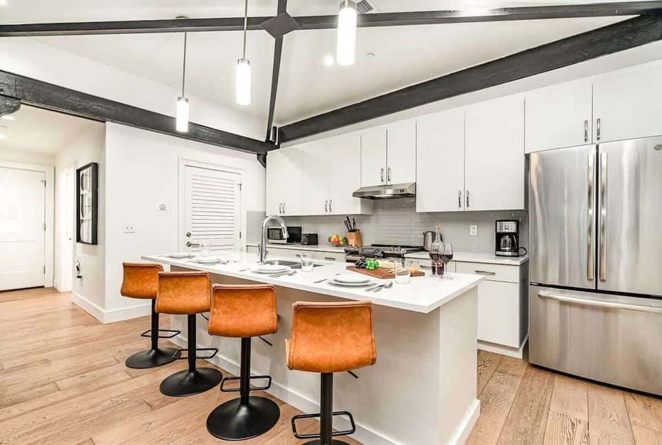 Kitchen with stainless steel appliances, white cabinetry and countertops, and kitchen island with bar seating for 4 guests.