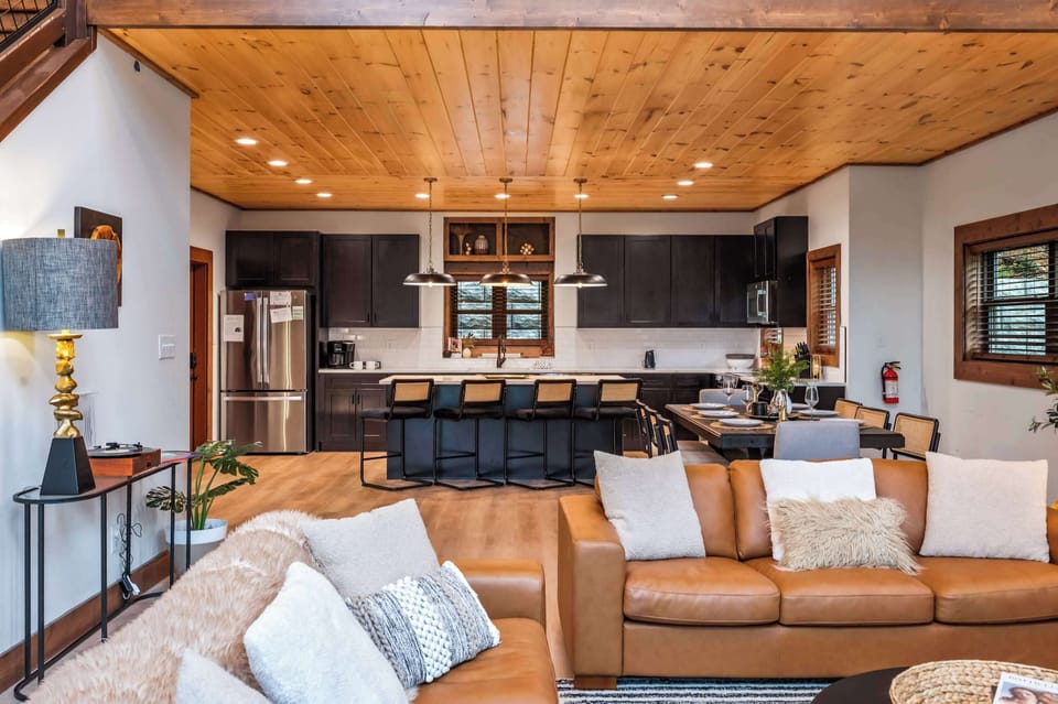 Open-concept living area with leather sofas and a modern kitchen featuring a wooden ceiling.