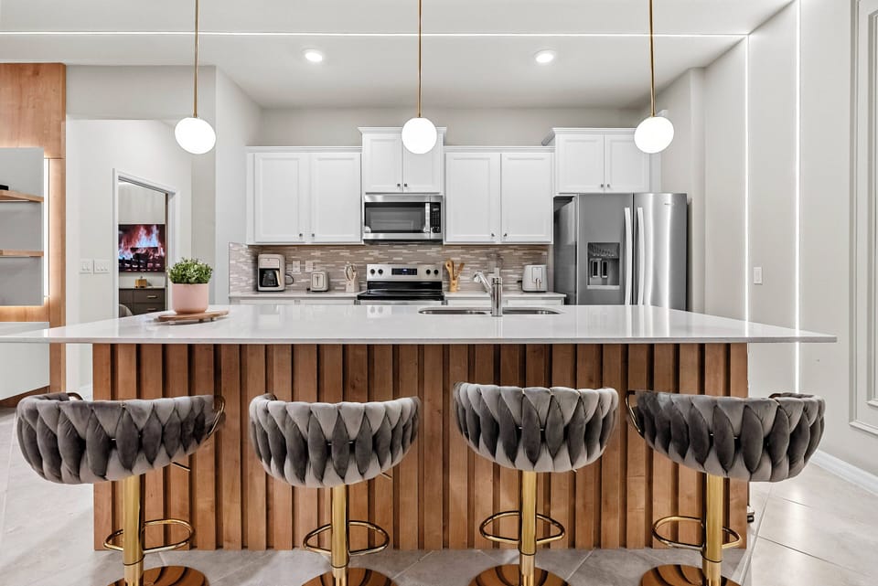 Welcome to this stylish kitchen, where sleek white cabinetry meets warm wood accents. The inviting island, complete with modern bar stools, is perfect for casual dining or savoring your morning coffee under chic pendant lights.