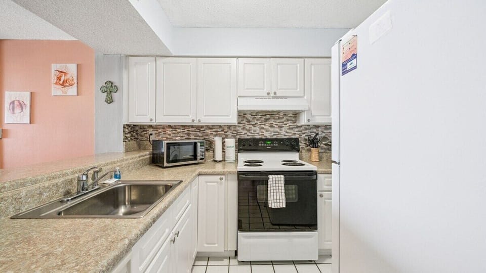Fully equipped kitchen with white cabinetry, mosaic tile backsplash, stove, microwave, and full-size refrigerator—perfect for vacation meals.