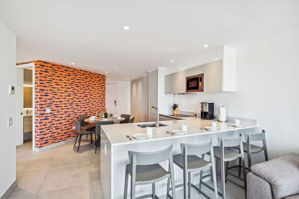 Your spacious modern kitchen awaits with sleek countertops, contemporary dining seating, and striking orange accent wall. Fully equipped for meal prep and leisurely breakfasts together.