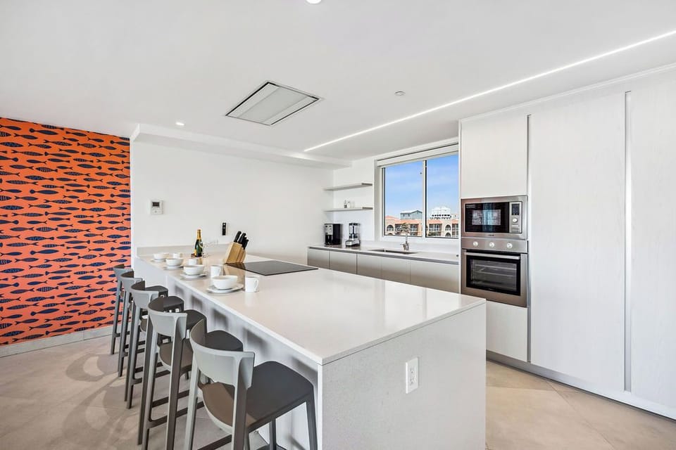 Step into this bright, modern kitchen where sleek white cabinetry and gleaming countertops invite you to whip up your favorite meals together.