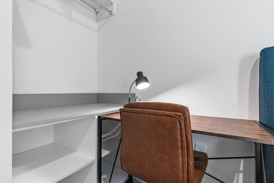 Enjoy a cozy workspace with a stylish brown chair and a sleek industrial desk, ideal for catching up on emails or planning your next adventure, all enhanced by soft lighting that invites you to settle in comfortably.
