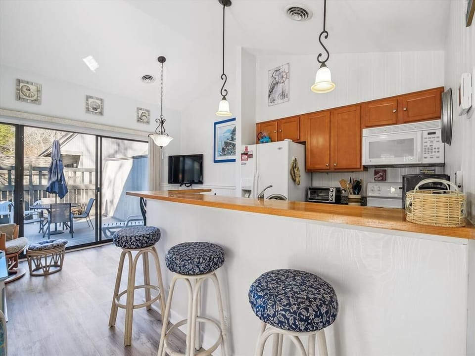 Inside, the inviting kitchen features warm wooden cabinetry, a breakfast bar with stylish stools, and seamless access to the adjoining deck, perfect for entertaining.