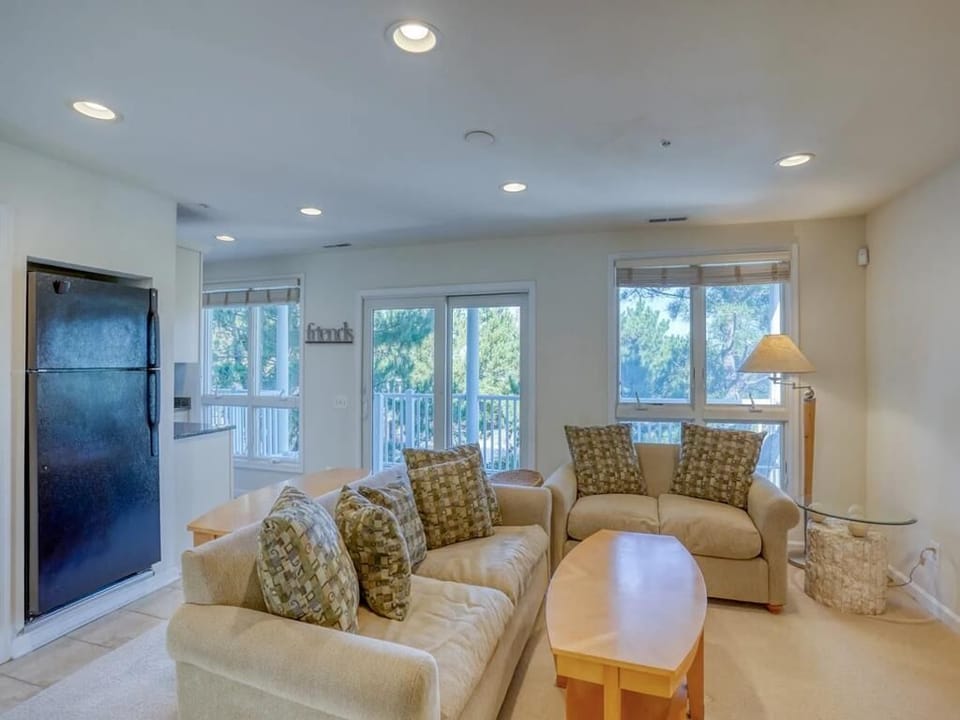 The cozy living room features plush seating and large windows that drench the space in natural light while offering serene views of the surrounding greenery.