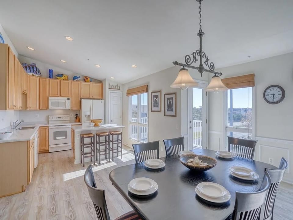 The spacious dining area, bathed in sunlight, features a charming table set for gatherings, complemented by an open kitchen that fosters a warm and social environment, perfect for enjoying meals together.