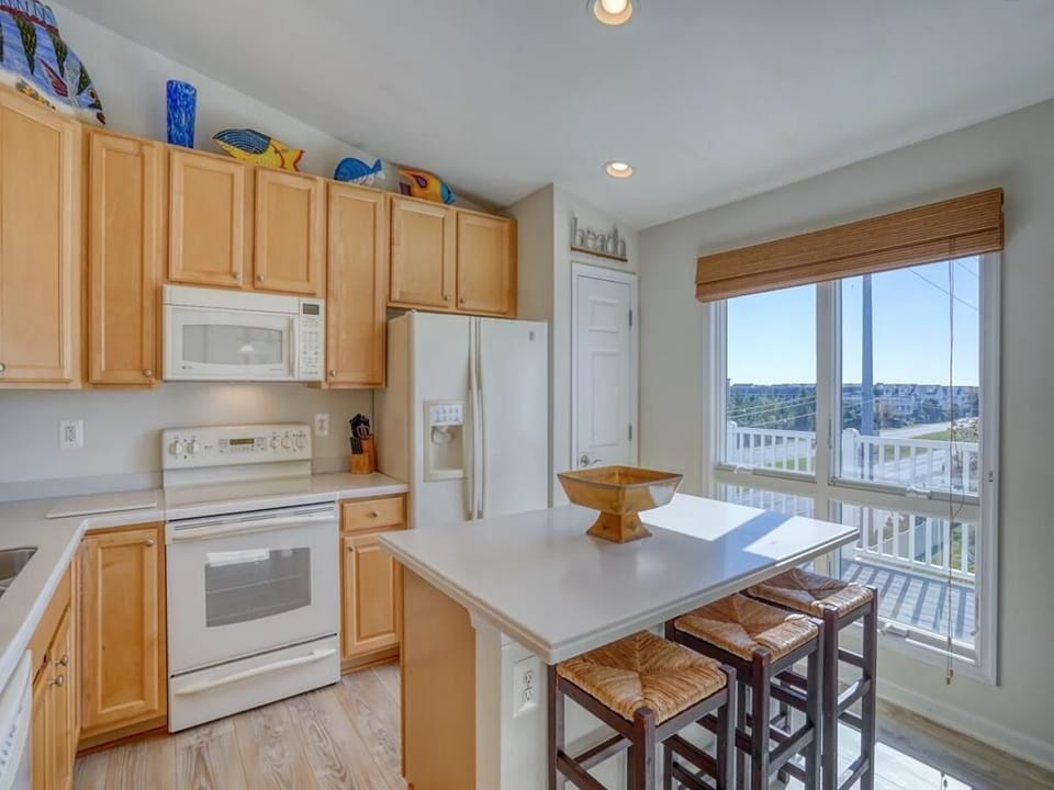 This airy kitchen features a modern layout with warm wood cabinetry, sleek countertops, and an inviting breakfast bar that overlooks ocean views through large windows.
