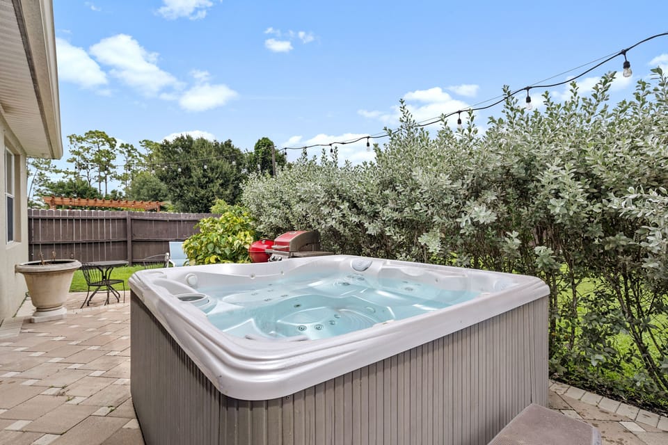 Outdoor hot tub on a brick paver patio flanked by greenery and string lights.