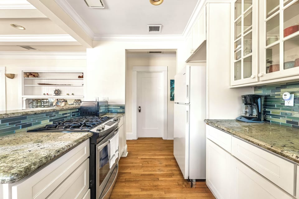 Bright galley kitchen with granite, gas range, coffee bar, and glass tile.