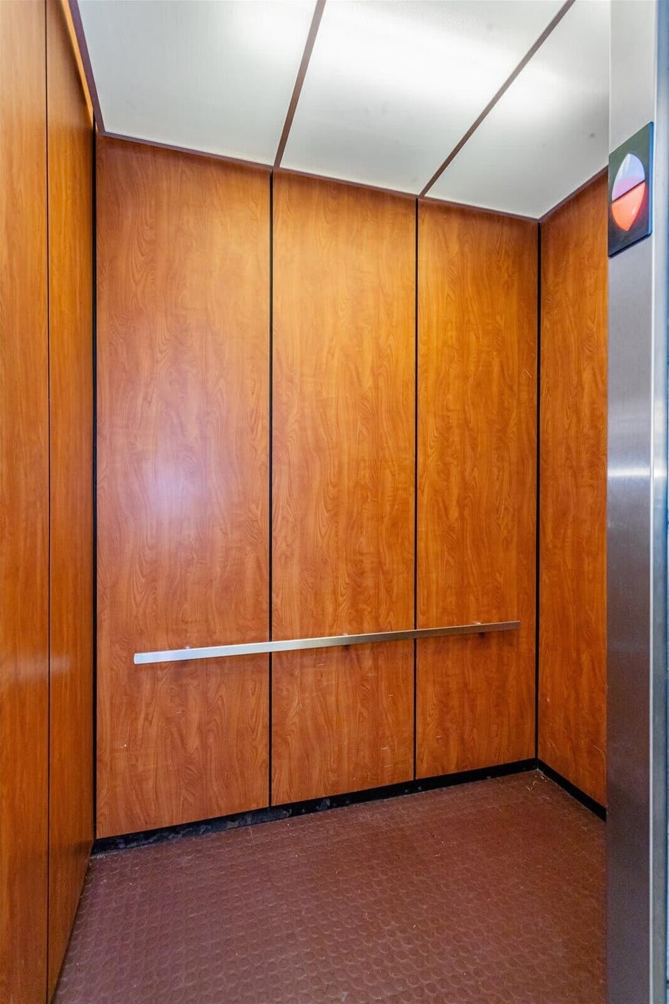 Elevator interior with wood paneling and metal handrail for convenient access.