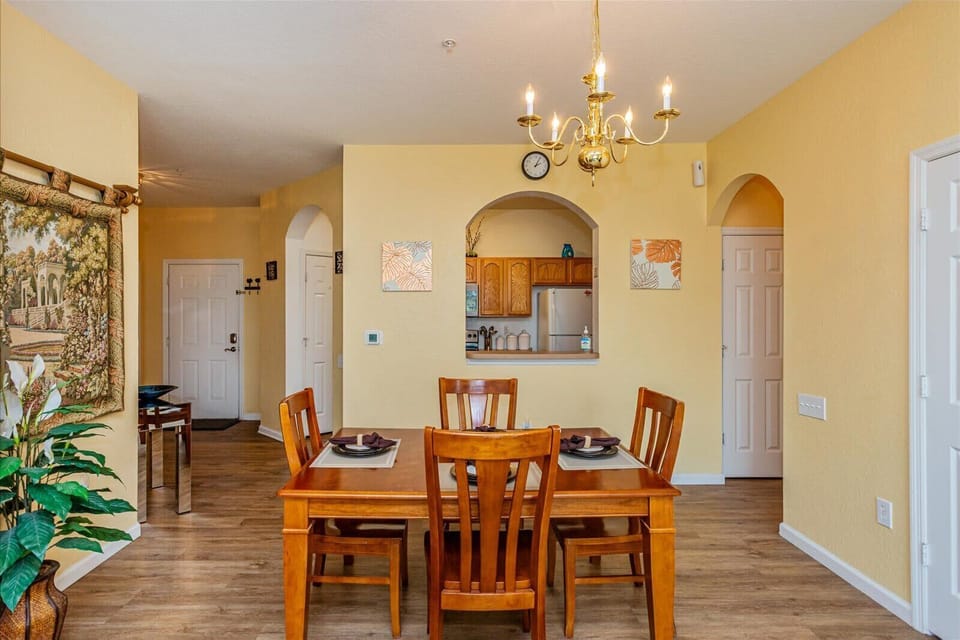 Dining area with wooden table and chandelier overlooking the kitchen through an arched pass-through