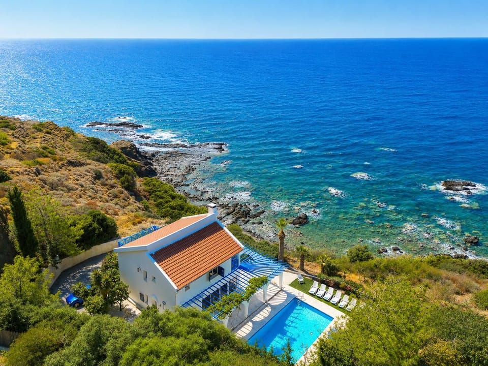Aerial seafront villa with a private pool, lush surroundings, and stunning panoramic ocean views.