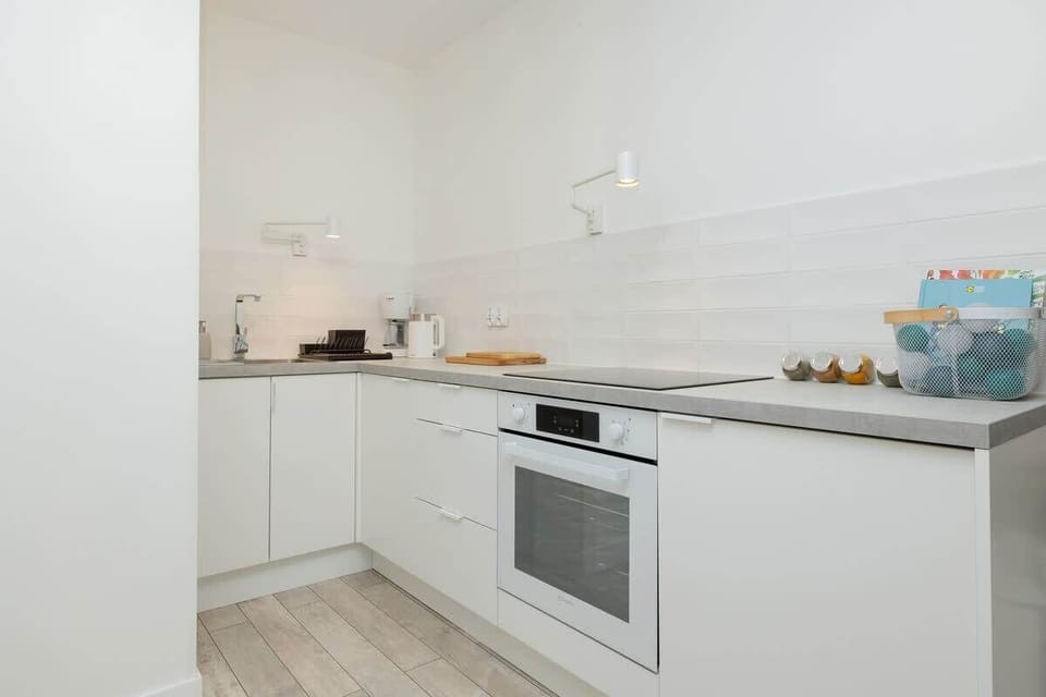 A modern white kitchen with built-in appliances, a flat cooktop, and minimalistic cabinetry.

