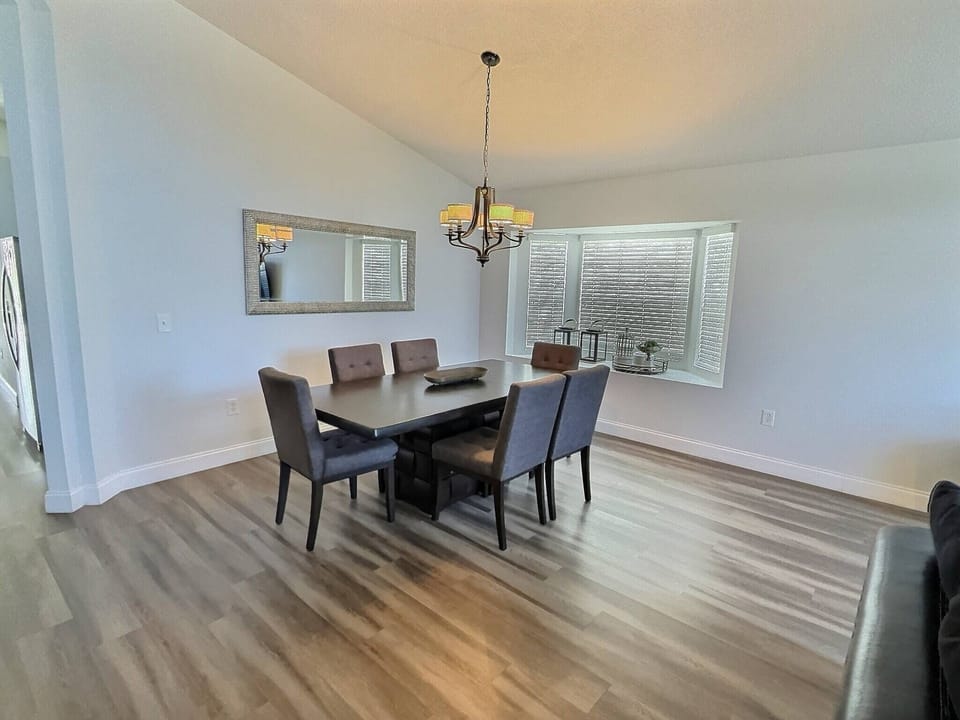 Enjoy shared meals in our stylish dining area with a wooden table and plush chairs, all illuminated by a beautiful chandelier that enhances the warm tones of the hardwood floor for an inviting atmosphere.
