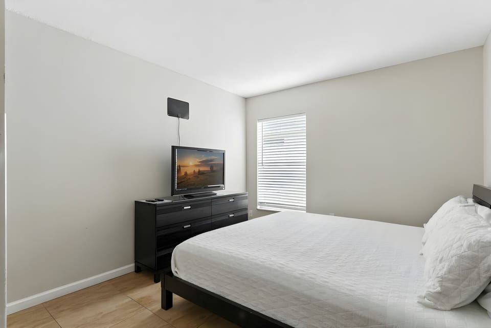 Enjoy the calming simplicity of this thoughtfully designed bedroom, featuring a plush queen bed and sleek black furniture for a contemporary touch. Natural light floods in, enhancing the inviting ambiance for your stay.
