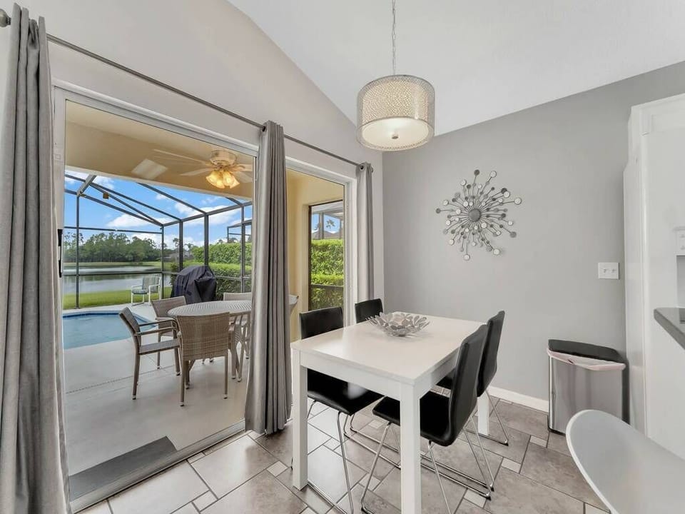 This bright dining nook boasts a sleek white table and modern black chairs, offering a stylish space for meals. Large sliding doors open to a lovely outdoor area, inviting fresh air and natural light for a delightful experience.