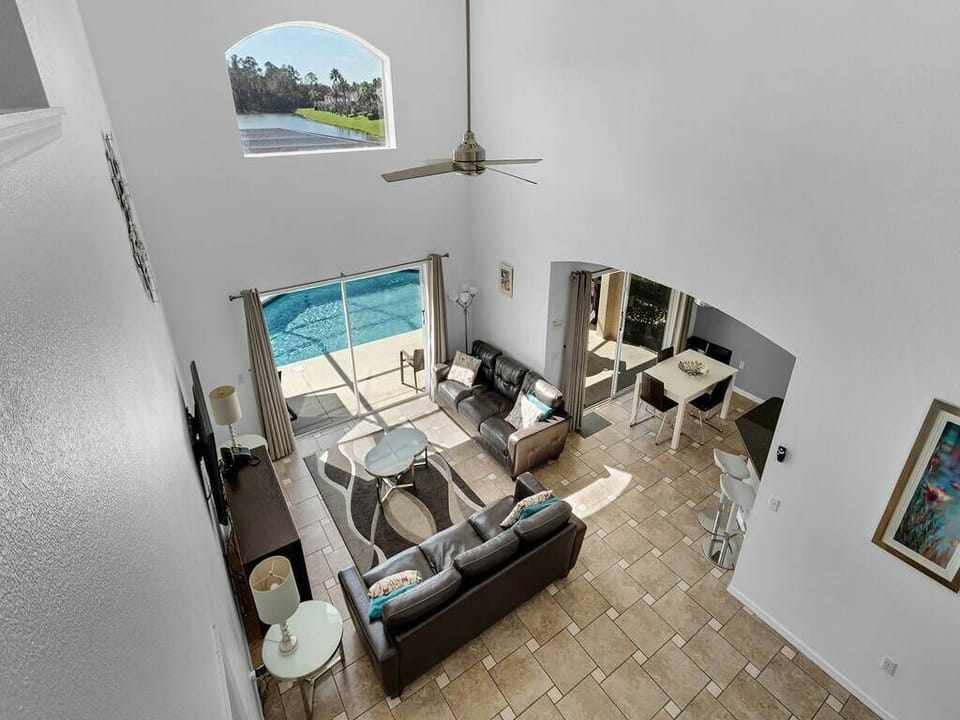 Take in the spacious living area bathed in natural light from large windows, showcasing warm tile floors and cozy gray seating, while enjoying easy access to the inviting pool area, ideal for relaxation and gatherings.