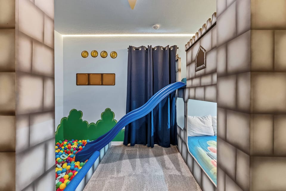 Step into a whimsical playroom, where a bright blue slide leads into a colorful ball pit, perfect for endless fun. The castle-themed decor combined with playful elements makes this space an adventure waiting to happen.
