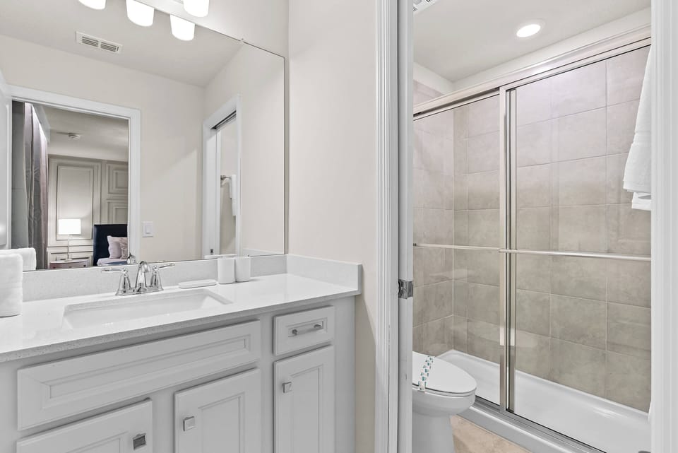 Step into a bright and airy bathroom featuring a sleek glass shower and a spacious vanity with elegant white cabinetry. The warm wooden flooring complements the neutral tile, creating a refreshing atmosphere for your stay.