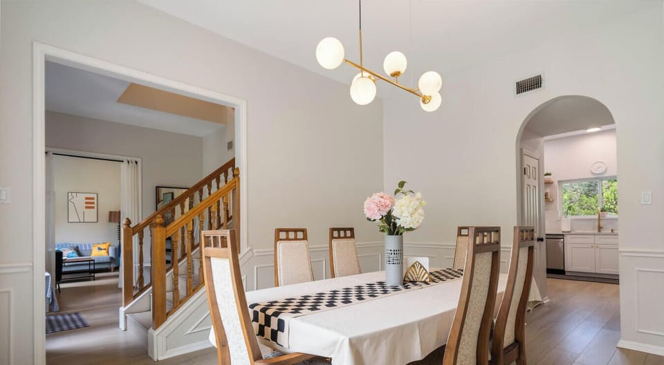 Dining table, center stage. Flowers fluffed, runner crisp, kitchen clinks cue the next scene.