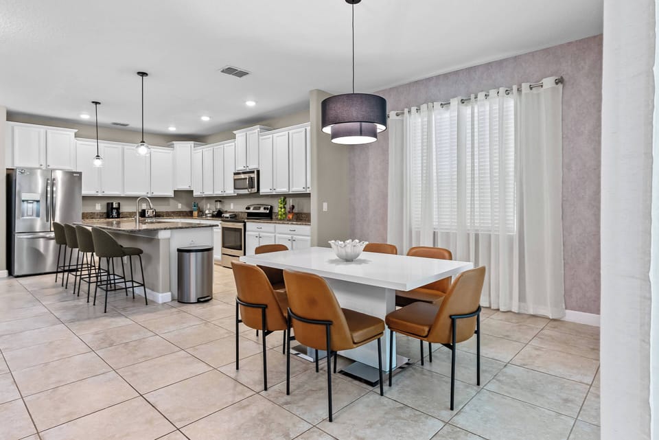 Experience mealtime bliss in this bright kitchen-dining area, featuring a sleek white table surrounded by stylish tan chairs. The modern cabinetry and soft lighting create a warm ambiance, while large windows invite natural light.