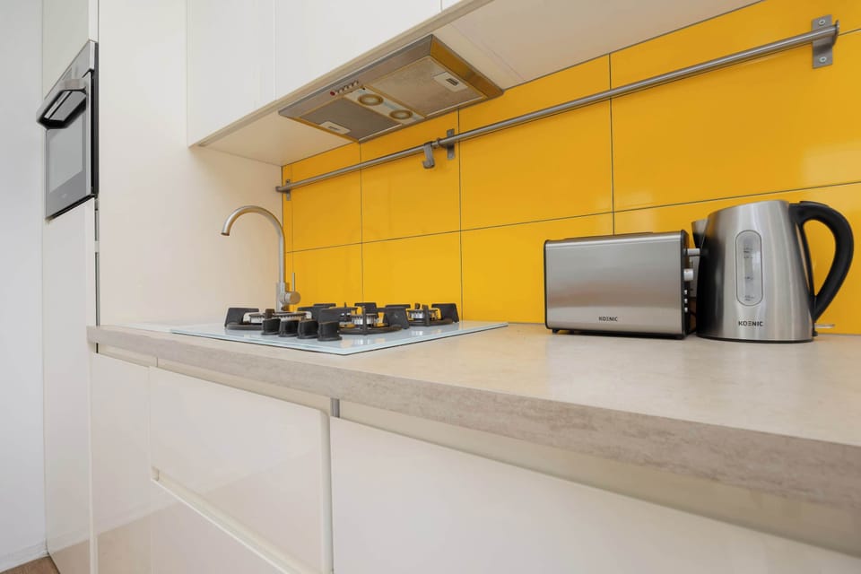 A narrow kitchen corner featuring yellow cabinetry and a stove with clean white backsplash and wooden countertop.