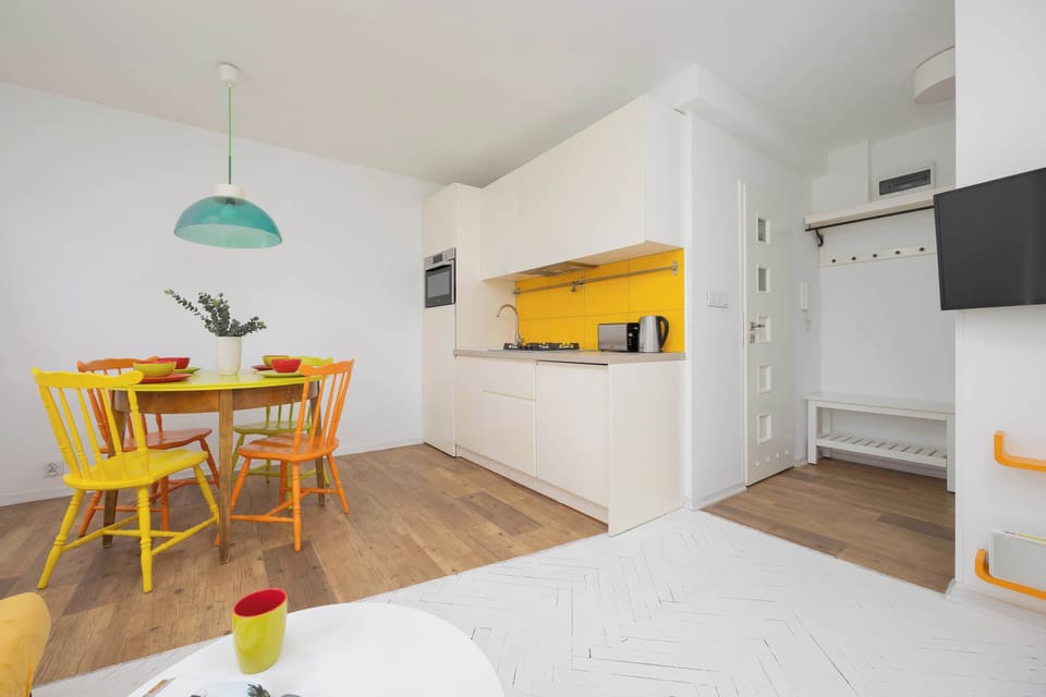 A modern kitchen and dining space with yellow cabinets, a green hanging lamp, and a wood dining set. The room is compact yet inviting.