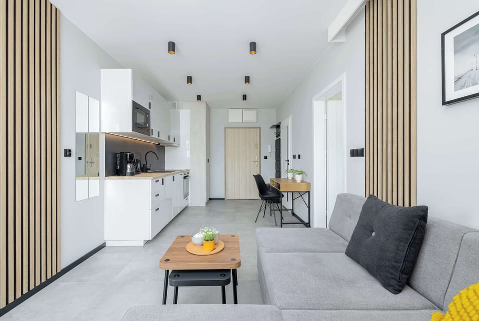 A modern kitchenette open to the living room, with white minimalist furniture and high-end appliances (refrigerator, dishwasher, oven), encourages cooking together.