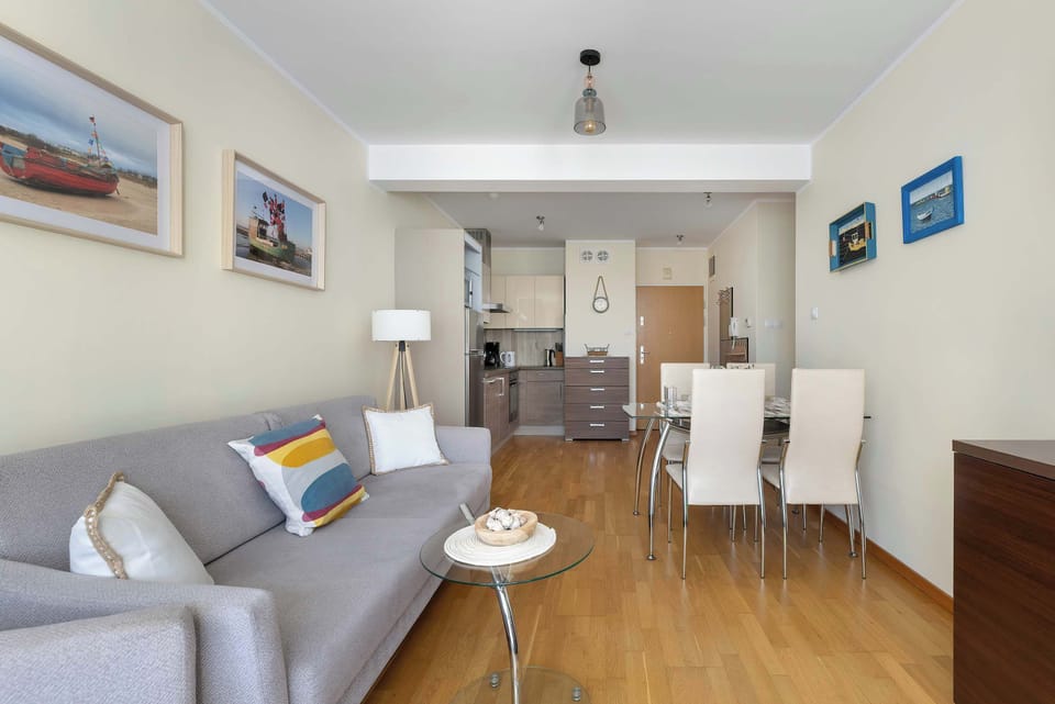 A living room corner shows a sofa and a small dining table near the window. Framed artwork on the walls adds a subtle decorative touch.
