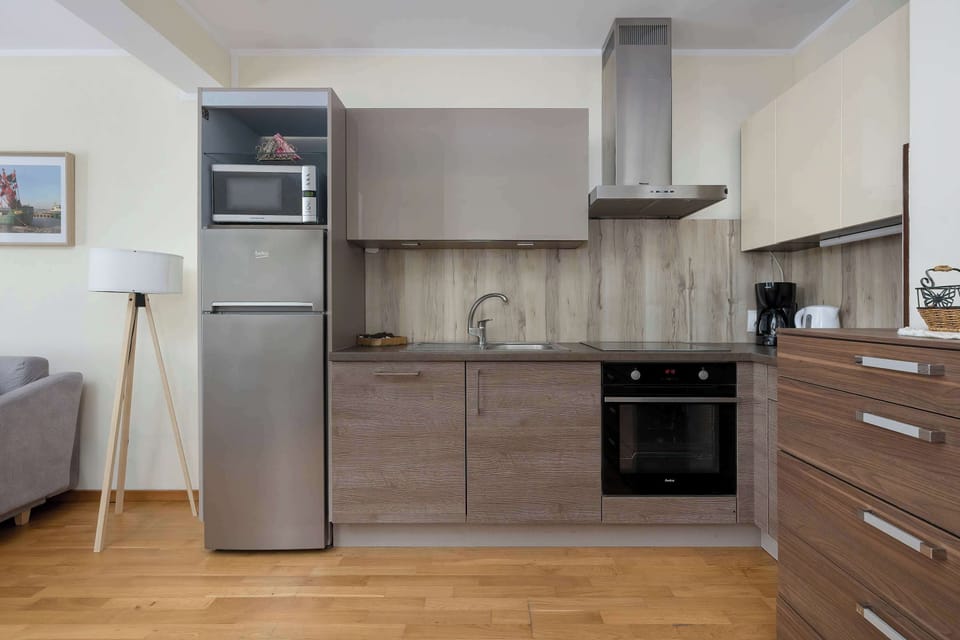 A modern kitchen includes stainless steel appliances, wooden cabinets, and a clean countertop. The layout is simple and functional with plenty of storage.