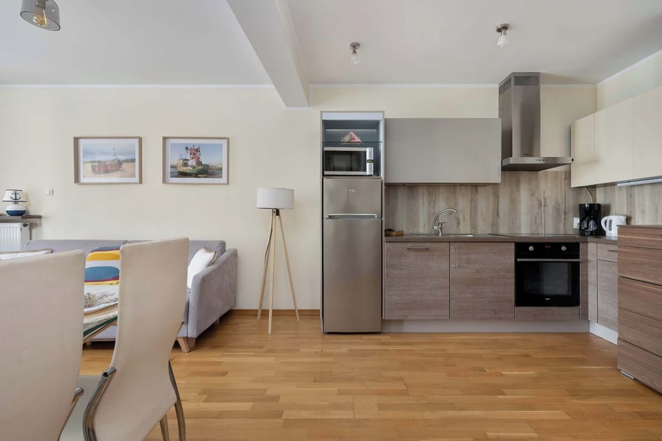 A studio-style interior shows a bed placed near the kitchen area. Light colors and minimal furnishings make the space feel open.